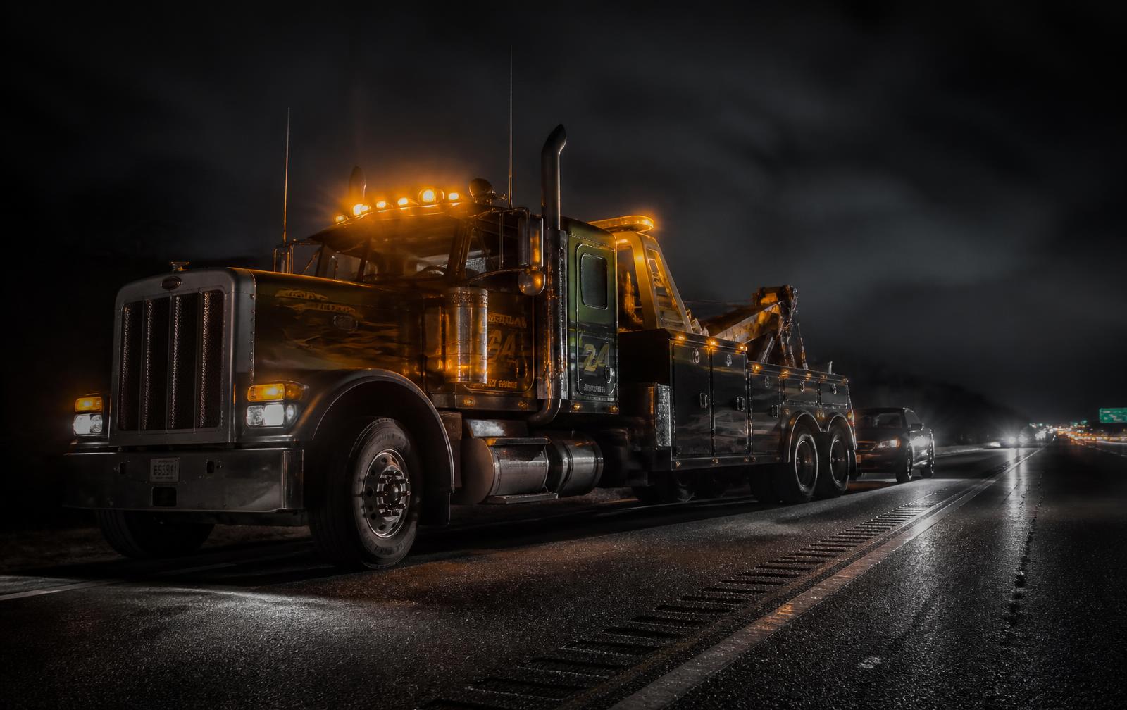 Heavy duty wrecker parked on a highway shoulder at night with amber lights running
