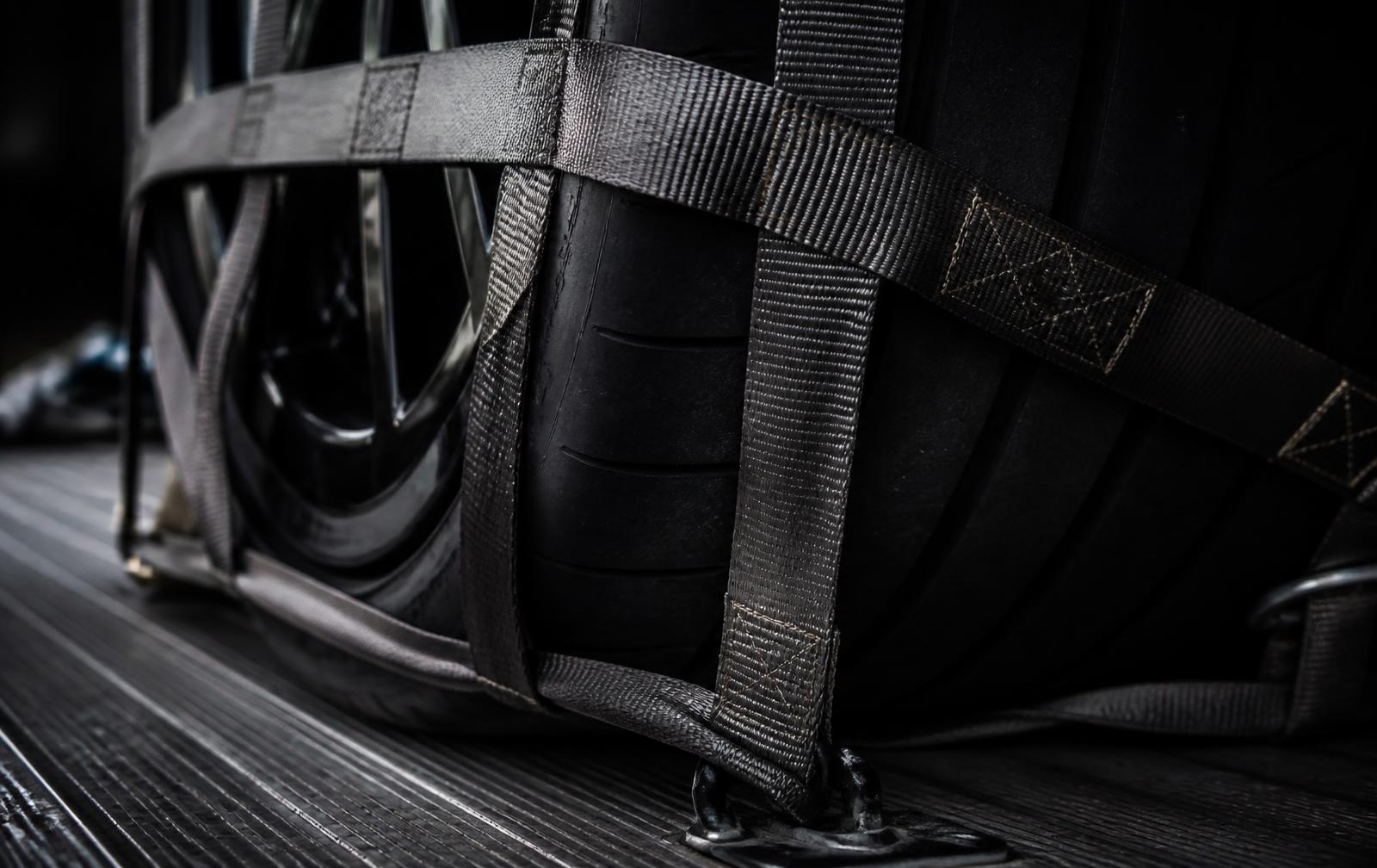 Close view of soft straps and a wheel net securing a performance car tire to a flatbed deck